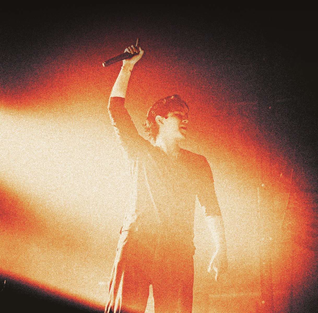 Ian Asher performing live, arm raised with microphone under warm stage light