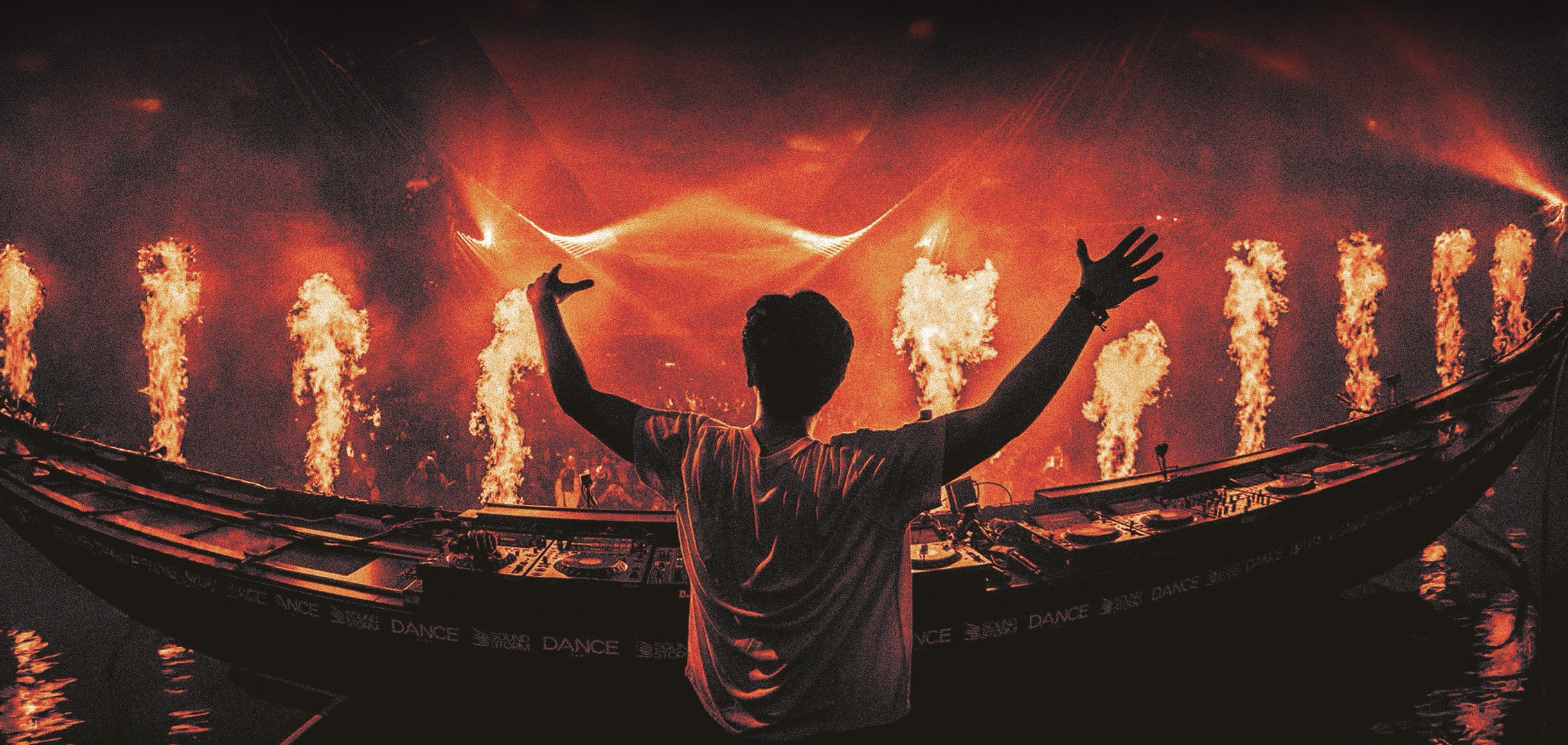 Ian Asher arms outstretched at the decks in front of pillars of pyro